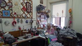 Pokaż zdjęcie: pomieszczenie w którym prowadzone są warsztaty krawieckie. Przy maszynie krawieckiej siedzi uczestniczka warsztatów i szyje poduszki na prezenty