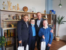 Czterech mężczyzn pozuje do zdjęcia, starszy wyższy stoi z tyłu i obejmuje trzech stojących przed nim. Uśmiechają się.