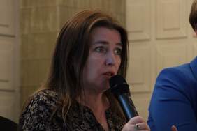 Pokaż zdjęcie: Zdjęcie kobiety z długimi ciemnymi włosami, ujęcie do wysokości ramiom, trzymającej w ręku mikrofon