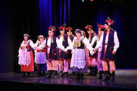 Pokaż zdjęcie: Na scenie duża grupa tancerzy tańczy w strojach ludowych.