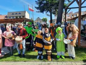 Pokaż zdjęcie: Na trawie stoi grupa dzieci. Są przebrane za różne zwierzęta. Niektórzy trzymają w dłoniach bębny. 