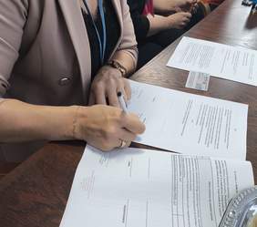 Pokaż zdjęcie: Zdjęcie dokumentu umowy i zbliżenie ręki osoby podpisującej umowę.