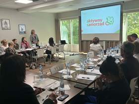 Sala konferencyjna. Uczestnicy siedzą przy stolikach i słuchają prelegenta. Na ekranie wyświetlane są procedury programu PFRON.