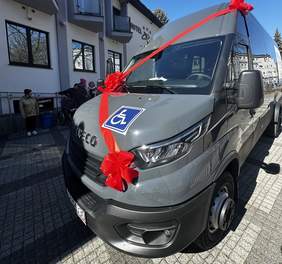 Pokaż zdjęcie: Zdjęcie przodu autobusu przystosowanego do przewozu osób z niepełnosprawnościami. Autobus udekorowany jest czerwoną kokardą.