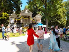 Pokaż zdjęcie: Podczas występu jednej z grup artystycznych, kilka osób tańczy na trawie, dobrze się bawiąc.