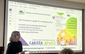 Pokaż zdjęcie: Osoba prowadząca prezentację stoi obok ekranu wyświetlającego slajd dotyczący wykorzystania gogli VR w urzędzie pracy oraz informacji kontaktowych Centrum Poradnictwa Zawodowego w Białymstoku.