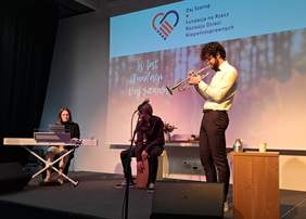 MIni recital - trzech wykonawców występuje na scenie, grając na instrumentach