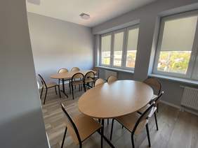 Pokaż zdjęcie: świetlica, dwa stoły z krzesłami, pomieszczenie przestronne z dużą ilością okien