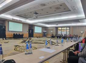 Pokaż zdjęcie: Sala konferencyjna. Dookoła sali ustawione są stoły przy których siedzą uczestnicy konferencji.