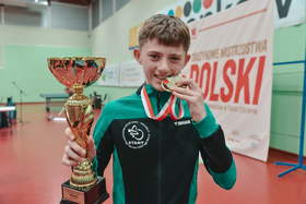 Młody chłopak z medalem w zębach i złotym trofeum w rękach