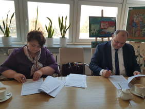 mężczyzna i kobieta siedzą w pokoju nad jasnym stołem, pochylają się i podpisują dokumenty