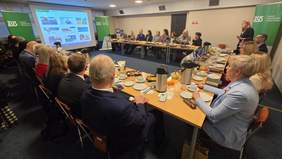 Grupa kilkunastu osób, kobiety i mężczyźni, siedzą za stołem