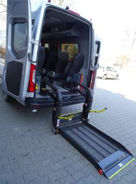 Pokaż zdjęcie: prezentowanie autobusu do przewozu uczestników Środowiskowego Domu Samopomocy. Na zdjęciu tylna część samochodu która pokazuje windę umożliwiającą wjazd  osoby na wózku