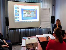 Pokaż zdjęcie: salka konferencyjna na której widnieje rzutnik z prezentacją projektu kompleksowej rehabilitacji na sali siedzą osoby które oglądają prezentację i słuchają informacji o projekcie