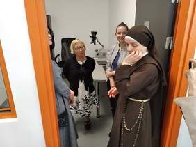 Pokaż zdjęcie: cztery osoby rozmawiają w pokoju. W tle sprzęty komputerowe