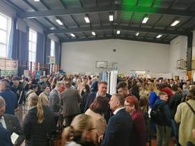 Zdjęcie sali gimnastycznej na której odbywają się targi, pomiędzy stoiskami chodzą osoby poszukujące pracy oraz wystawcy.