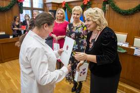 naśrodku sali Pani Pniewska wręcza Certyfikat i upominek jednej z uczestniczek sejmiku, w tle widać dwie kolejne kobiety