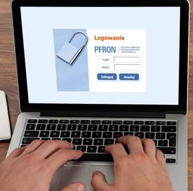 Pokaż zdjęcie: Dłonie mężczyzny położone są na klawiaturze laptopa. Na ekranie laptopa widoczny jest ekran startowy logowania do Systemu Obsługi Dofinansowań i Refundacji. Ekran startowy zawiera następujące sformułowania: „Logowanie”, „PFRON”, „System Obsługi Dofinansowań i Refundacji”, „Login”, „Hasło”, „Zaloguj” oraz „Anuluj”. Ponadto po lewej stronie umieszczona została szara kłódka.