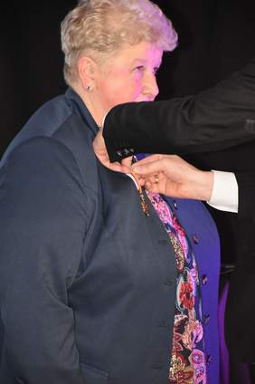 Pokaż zdjęcie: Kobiecie, blondynce po prawej przypinany jest honorowy medal.