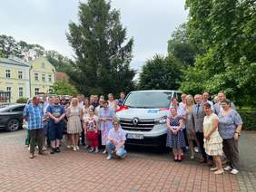 Pokaż zdjęcie: Grupa osób stoi wokół busa przyozdobionego kokardą