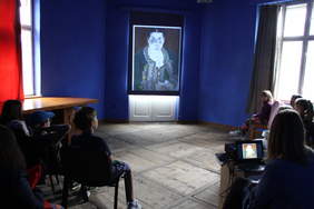 Pokaż zdjęcie: Dzieci podczas zajęć w "Szafirowej pracowni" - dzieci oglądają film wyświetlony na ekranie, w tle niebieska ściana