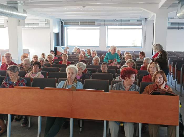 Pokaż zdjęcie: Na sali wykładowej na krzesłach siedzą seniorzy, którzy przyszli na spotkanie