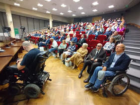 Pokaż zdjęcie: Sala konferencyjna, układ krzeseł jak kinie w rzędach wznoszących się coraz wyżej, kilkudziesięciu uczestników