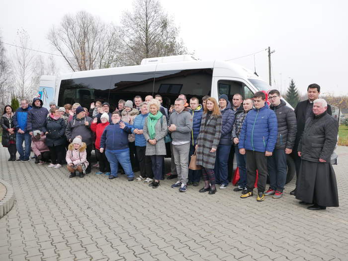 Pokaż zdjęcie: Uczestnicy WTZ, kadra oraz zaproszeni goście stoją na tle białego, nowego pojazdu.