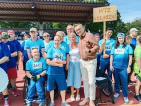 Pokaż zdjęcie: Drużyna czeka na rozpoczęcie olimpiady. Zawodnicy są ubrani w niebieskie koszulki. Jeden mężczyzna pokazuje kciuk w górę. 