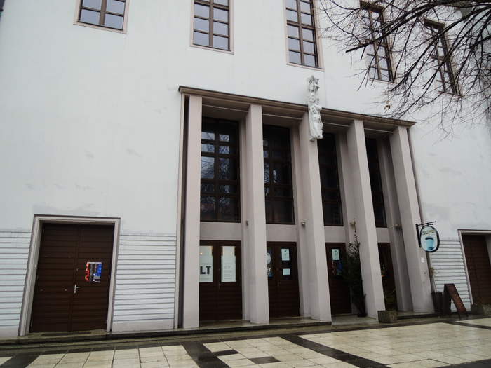 Pokaż zdjęcie: Front gmachu Lubuskiego Teatru w Zielonej Górze, są kolumny, ornamenty, widać zielonogórski deptak