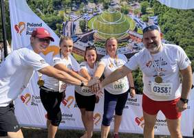 Pokaż zdjęcie: Pięciu pracowników Oddziału (2 mężczyzn, 3 kobiety) z uśmiechem na twarzy przybijają piątkę.