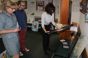 Pokaż zdjęcie: Zdjęcie korytarza biurowego, na krzesłach i podłodze poustawiane są prace plastyczne, komisja plastyczna przygląda się pracom, w skład komisji wchodzą trzy kobiety i mężczyzna