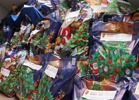 Pokaż zdjęcie: Na podłodze leży mnóstwo upominków i prezentów świątecznych. Naklejona jest na nich informacja, że są dofinansowane z Państwowego Funduszu Rehabilitacji Osób Niepełnosprawnych. 