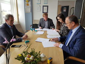 trzech mężczyzn i kobieta przy dużym jasnym stole podpisują dokumenty