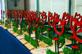 Pokaż zdjęcie: Na stole przykrytym niebieskim suknem stoją statuetki w kształcie tulipanów