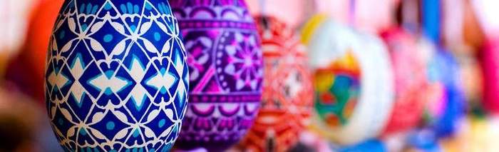 Pokaż zdjęcie: Pisanka wielkanocna malowana we wzory w kolorze w kolorze granatowym. W tle pisanki w innych kolorach.