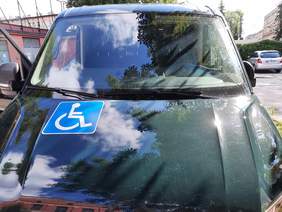 Pokaż zdjęcie: Na parkingu stoi zielony samochód przystosowany do przewozu osoby z niepełnosprawnością. 