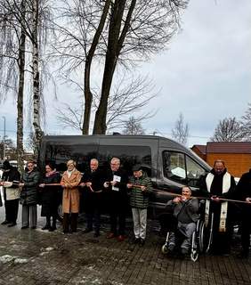 Pokaż zdjęcie: Uroczyste przecięcie wstęgi przed nowym mikrobusem przeznaczonym do przewozu osób z niepełnosprawnościami. W wydarzeniu uczestniczą przedstawiciele PFRON, samorządu oraz placówki, obok znajduje się osoba poruszająca się na wózku inwalidzkim. 