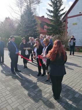 Przecinanie wstęgi, m.in. przez Panią Dyrektor Oddziału PFRON. Wokół stoi kilka osób, robią zdjęcia i przyglądają się.