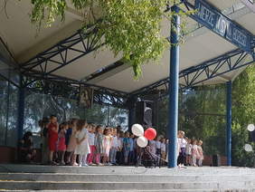 Pokaż zdjęcie: Na scenie stoi grupa małych dzieci. Nad nimi durze zadaszenie z napisem wierze w syna bożego.