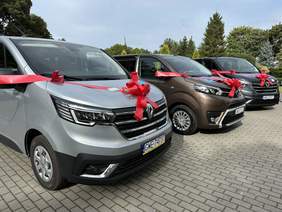 Pokaż zdjęcie: W rzędzie stoją trzy mikrobusy. Na maskach mają kokardę. W tle drzewa.