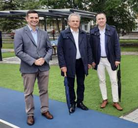 Pokaż zdjęcie: Na stadionie olimpijskim w Spale stoi trzech mężczyzn. Są elegancko ubrani w garnitury i uśmiechają się. 