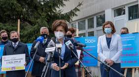 uczestnicy spotkania, zdjęcie w plenerze, na pierwszym planiepani minister przed mikrofonami, za nią 6 osób