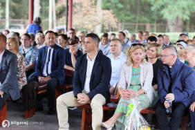 Pokaż zdjęcie: Zdjęcie zaproszonych gości siedzących na krzesełkach pod drewnianą wiatą.