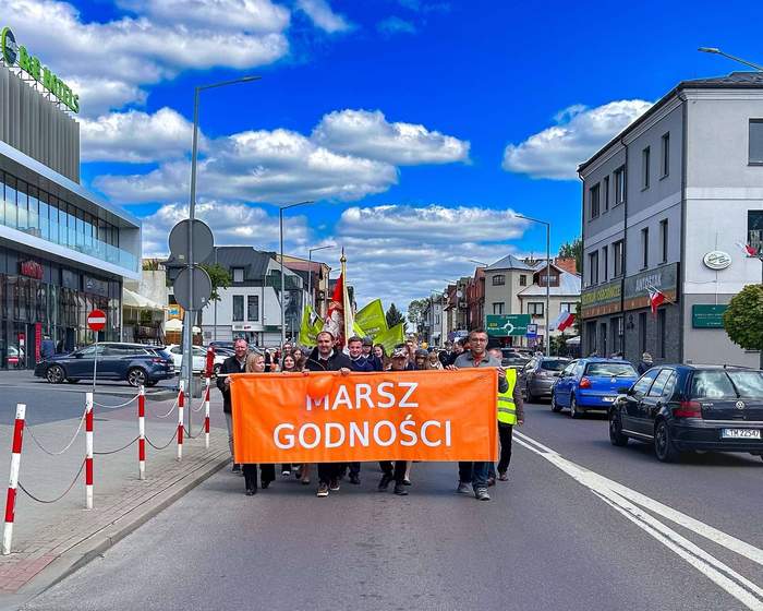 Pokaż zdjęcie: Pomarańczowy baner z napisem marsz godności. Baner trzymają uczestnicy marszu.