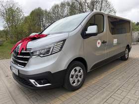 Srebrny bus do przewozu osób z niepełnosprawnościami stoi na parkingu. Na masce widoczna duża czerwona kokarda, a na drzwiach oznaczenia organizacji i Logo PFRON.