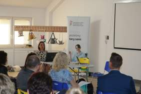 Pokaż zdjęcie: Siedząca przy biurku na którym postawiony jest laptop i rzutnik przedstawiciel PFRON pani Anna Światlak przedstawia zgomadzonym pracownikom PCPR zagadnienia związane z Systemem Obsługi Wsparcia.