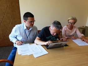 Pokaż zdjęcie: Opis grafiki: Na zdjęciu pracodawca i dwóch pracowników Oddziału. Siedzą przy stoliku, na którym stoi laptop i leżą dokumenty. Pracodawca pisze na komputerze.