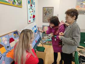 Pokaż zdjęcie: Kobiety oglądają prace plastyczne - kolorowe tkaniny zgłoszone w konkursie