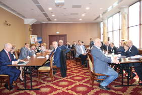 Pokaż zdjęcie: Na sali konferencyjnej uczestnicy siedzące przy stole konferencyjnym ustawionym w kształcie litery U